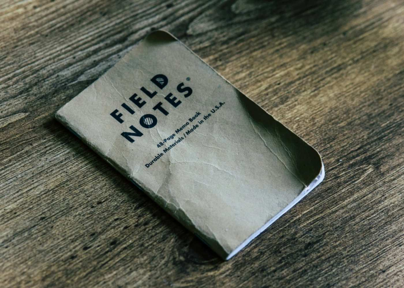 Field Notes notebook, wrinkled and worn, lays on a wooden tabletop. Photo by Kolby Milton on Unsplash.